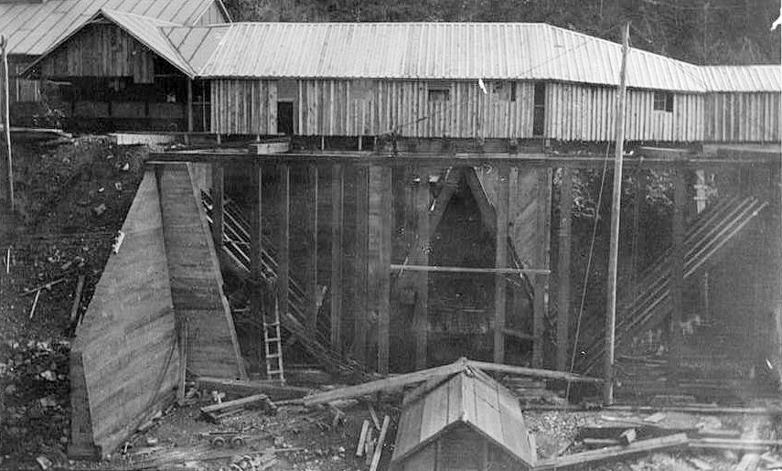 Bald Mountain Gold Mill, Lead South Dakota TROJAN MILL, DETAIL OF CRUDE ORE BINS FROM NORTH, c. 1912. SHOWS TIMBER FRAMING UNDER CONSTRUCTION FOR EAST AND WEST CRUDE ORE BINS AT PREVIOUS LOCATION OF CRUSHER HOUSE, AND SNOW SHED PRESENT OVER SOUTH CRUDE ORE BIN WITH PHASE CHANGE IN SNOW SHED CONSTRUCTION INDICATED AT EAST END OF EAST CRUDE ORE BIN. THIS PHOTOGRAPH IS THE FIRST IMAGE OF THE MACHINE SHOP, UPPER LEFT CORNER
