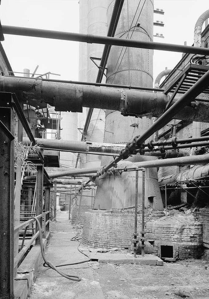 Sloss Furnace - Sloss-Sheffield Steel & Iron Company, Birmingham Alabama 1977 View looking east up walkway between blowing engine house at left and boilers at right showing base of stack for boilers No. 5 and 6.