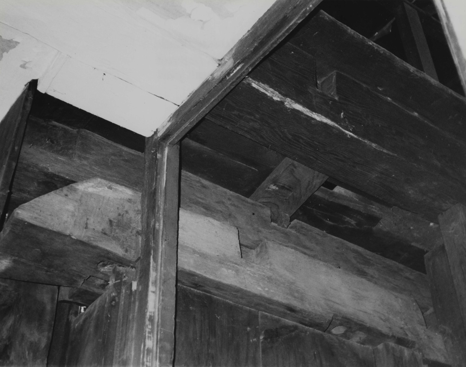 Dwight-Derby House, Medfield Massachusetts Detail of framing in attic stairwell, behind chimney stack, looking southwest. Ca. 1651 roof tie-beam (east end of original house) with sloped end, and west wall plate of adjacent (ca. 1669) room resting above (1999)
