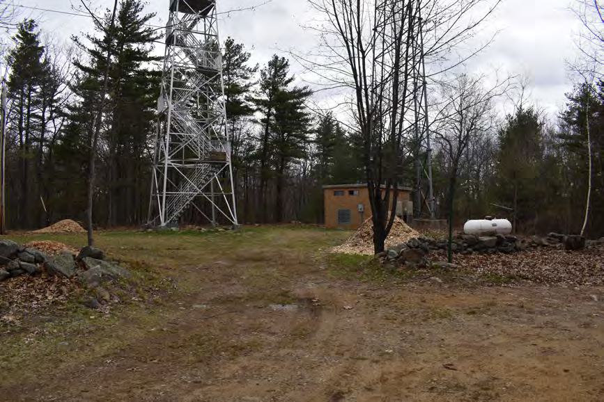 Warner Hill Fire Tower, Derry New Hampshire View of site from access road lined with stonewalls; fire tower, telecommunication building, and telecommunication tower, looking northeast (2022)