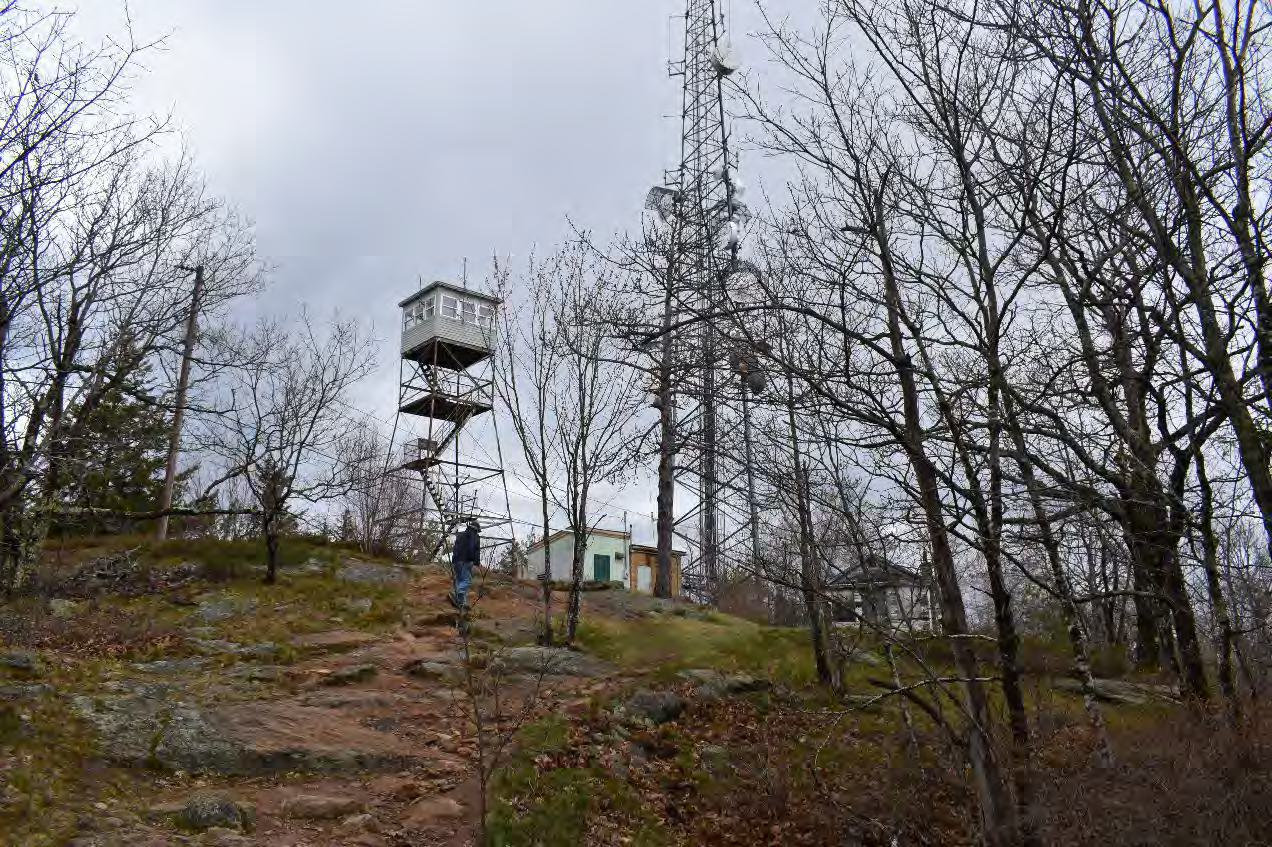 Blue Job Fire Tower, Farmington New Hampshire From left to right: telephone line, fire tower, telecommunication buildings and tower, and watchman's cabin, looking north from trail (2022)