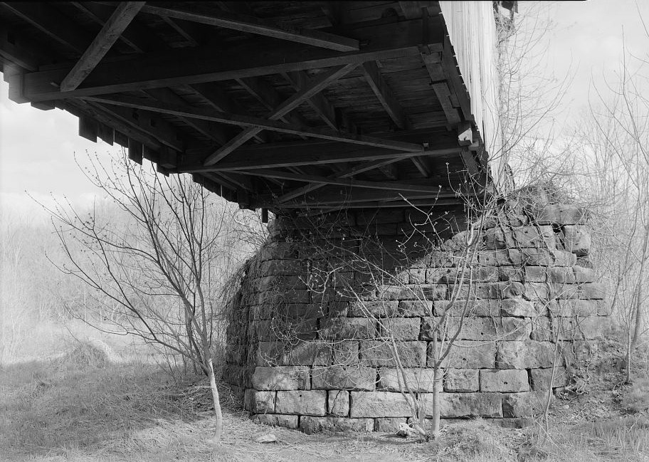 Crum Covered Bridge, Rinard Mills Ohio 2004 SOUTH ABUTMENT AND BELOW DECK DETAIL. NOTE THE FLOOR BEAMS ON THE APPROACH DO NOT REST ON THE LOWER CHORD BUT ARE SUSPENDED BELOW THE LOWER CHORDS BY MEANS LOOPED IRON HANGERS THAT WRAP AROUND WOODEN BLOCKS RESTING ON THE LOWER CHORD.