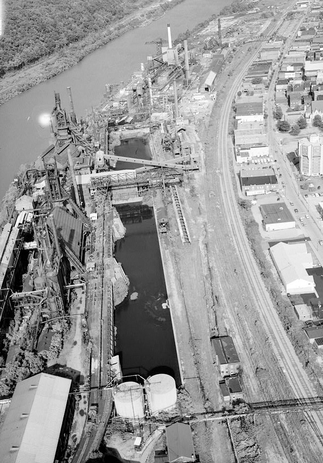 Pittsburgh Steel Company Monessen Works, Monessen Pennsylvania 1995 AERIAL VIEW FACING EAST, LOOKING DOWN CENTER OF ORE YARD. OIL TANKS IN FOREGROUND, ORE BRIDGE & SINTERING CONVEYOR IN CENTER, & COKE PLANT IN BACKGROUND.