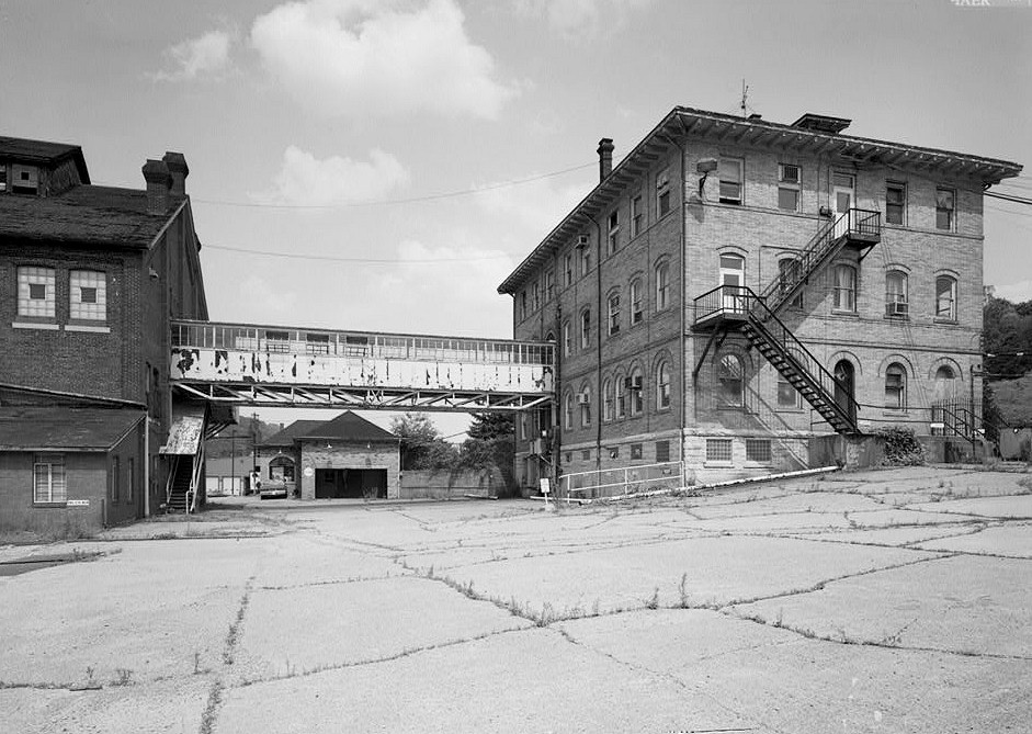 Pittsburgh Steel Company Monessen Works, Monessen Pennsylvania 1995 VIEW LOOKING EAST WITH MACHINE SHOP LEFT, GATE HOUSE CENTER (UNDER PEDESTRIAN BRIDGE), BETHLEHEM STEEL ADMINISTRATION BUILDING AT RIGHT.