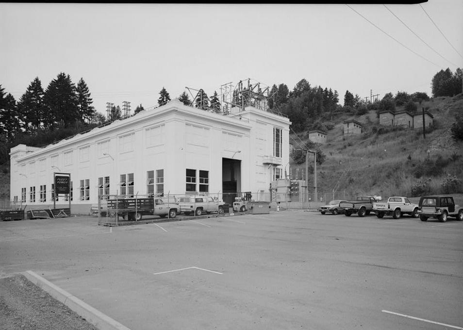 Puget Sound Power & Light Company, White River Hydroelectric Project, Dieringer Washington West and south facades of powerhouse, and abandoned lightning arrester houses on hillside above powerhouse; looking north (1989)