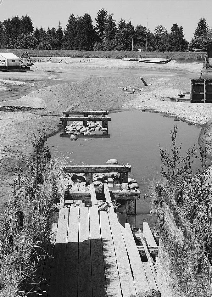 Electron Hydroelectric Project, Electron Washington LOOKING WEST FROM DETERIORATED END OF FLUME AT RESERVOIR'S EAST EDGE, SHOWING DREDGE IN LEFT BACKGROUND, SIDE VIEW OF FOREBAY SHED ON RIGHT (1984)